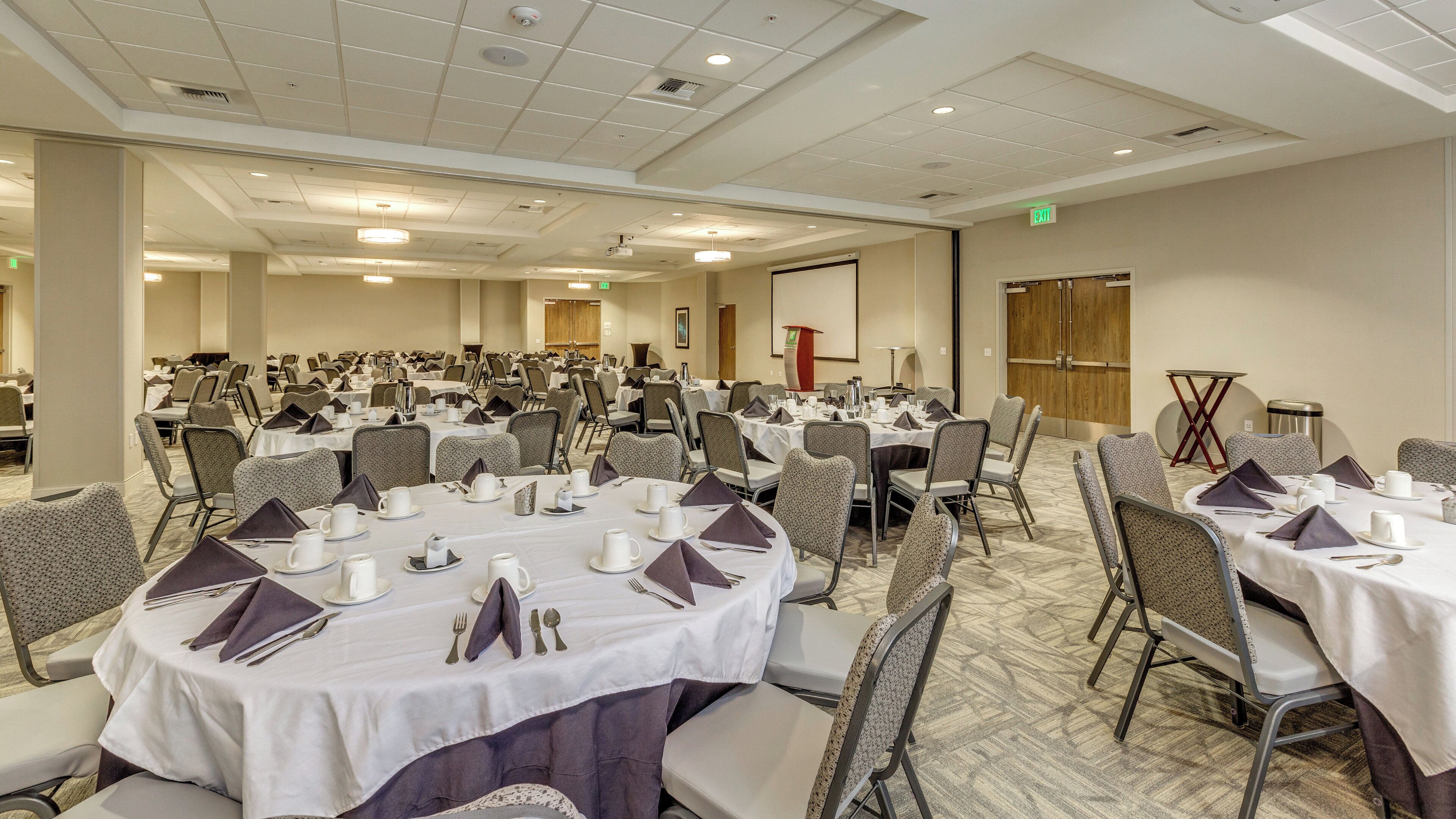 A conference room with multiple tables set for a meeting, equipped with chairs, tables, and presentation screens.