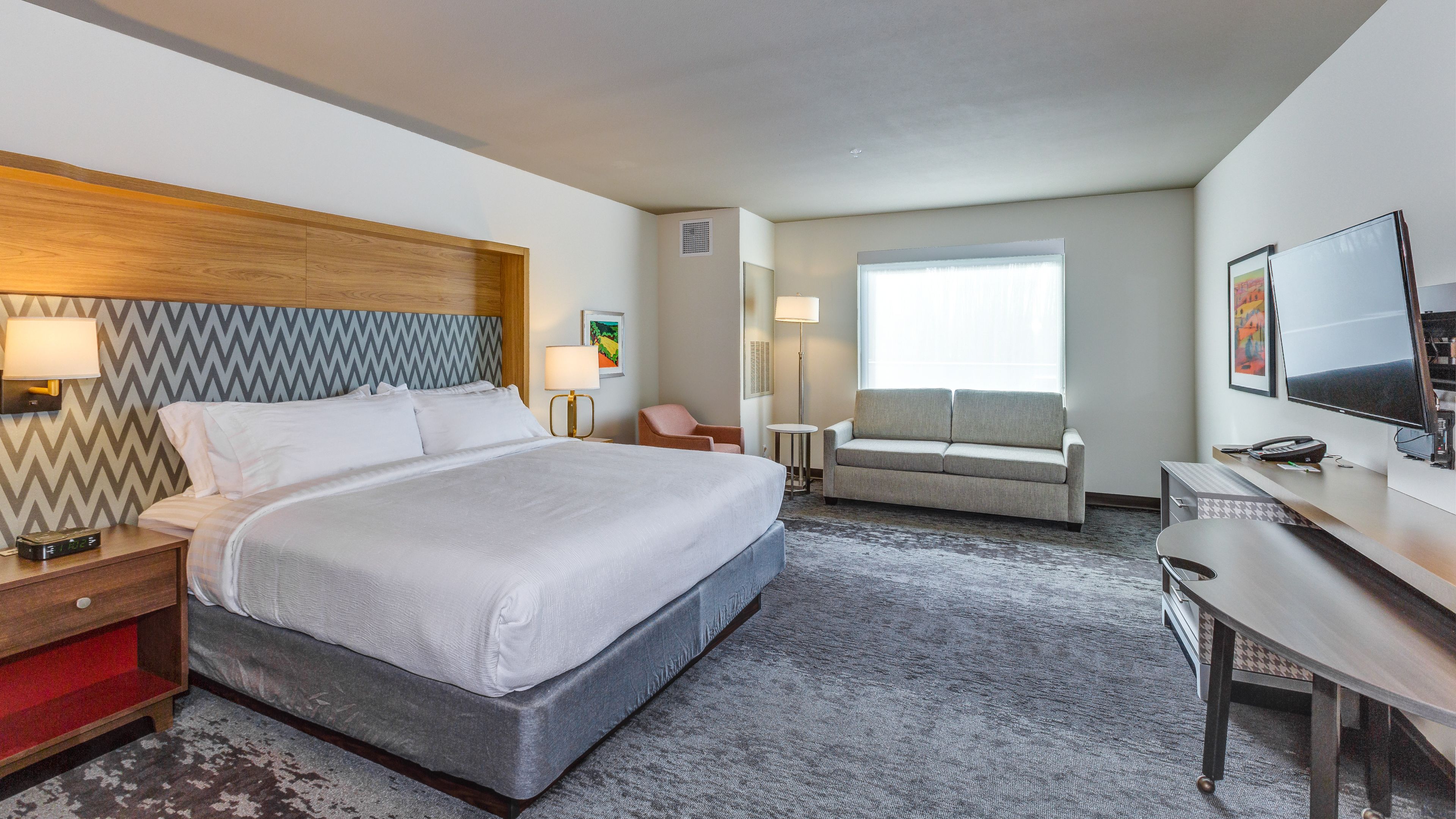 A hotel room with a large bed, a desk, a sofa, and a TV.