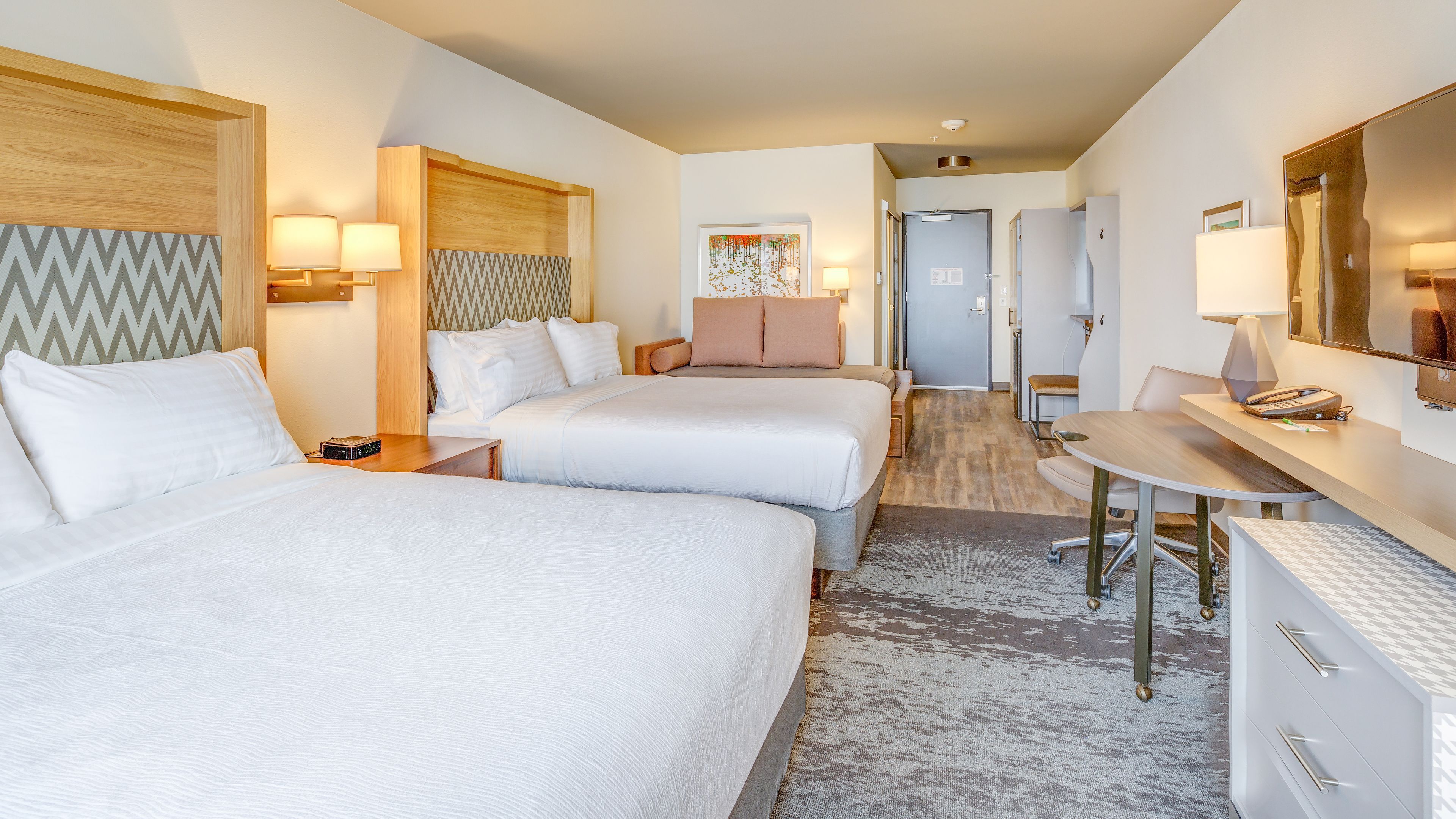 Une chambre d’hôtel avec deux lits, un bureau, une chaise, un miroir et une porte donnant sur une salle de bain.