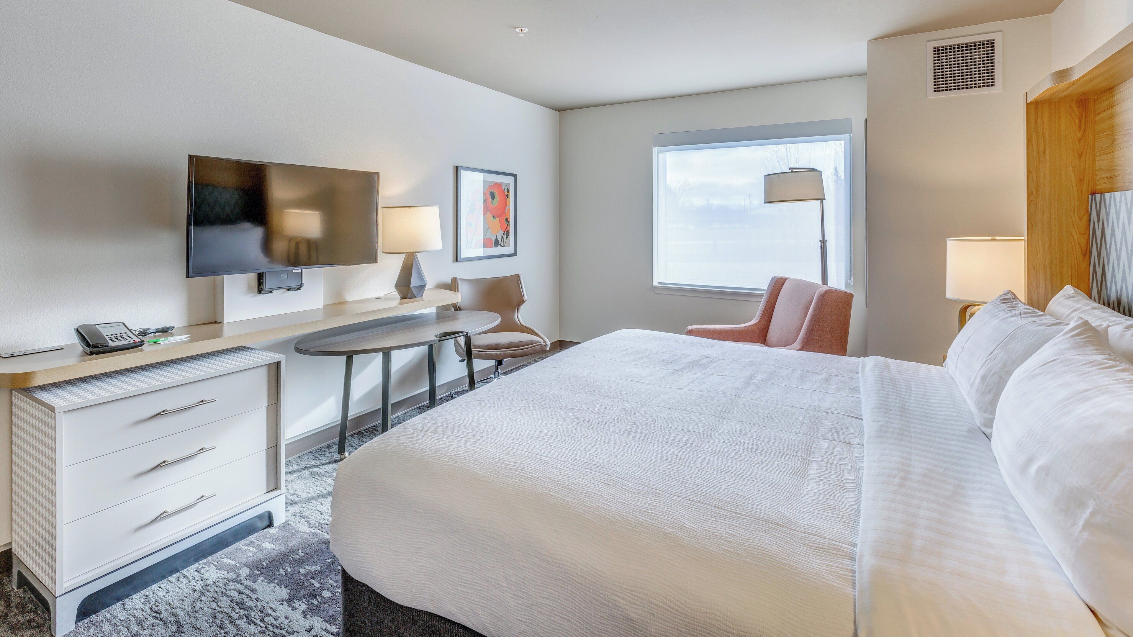 Ein Hotelzimmer mit Bett, Schreibtisch, Stuhl, Fernseher und Kunstwerken.