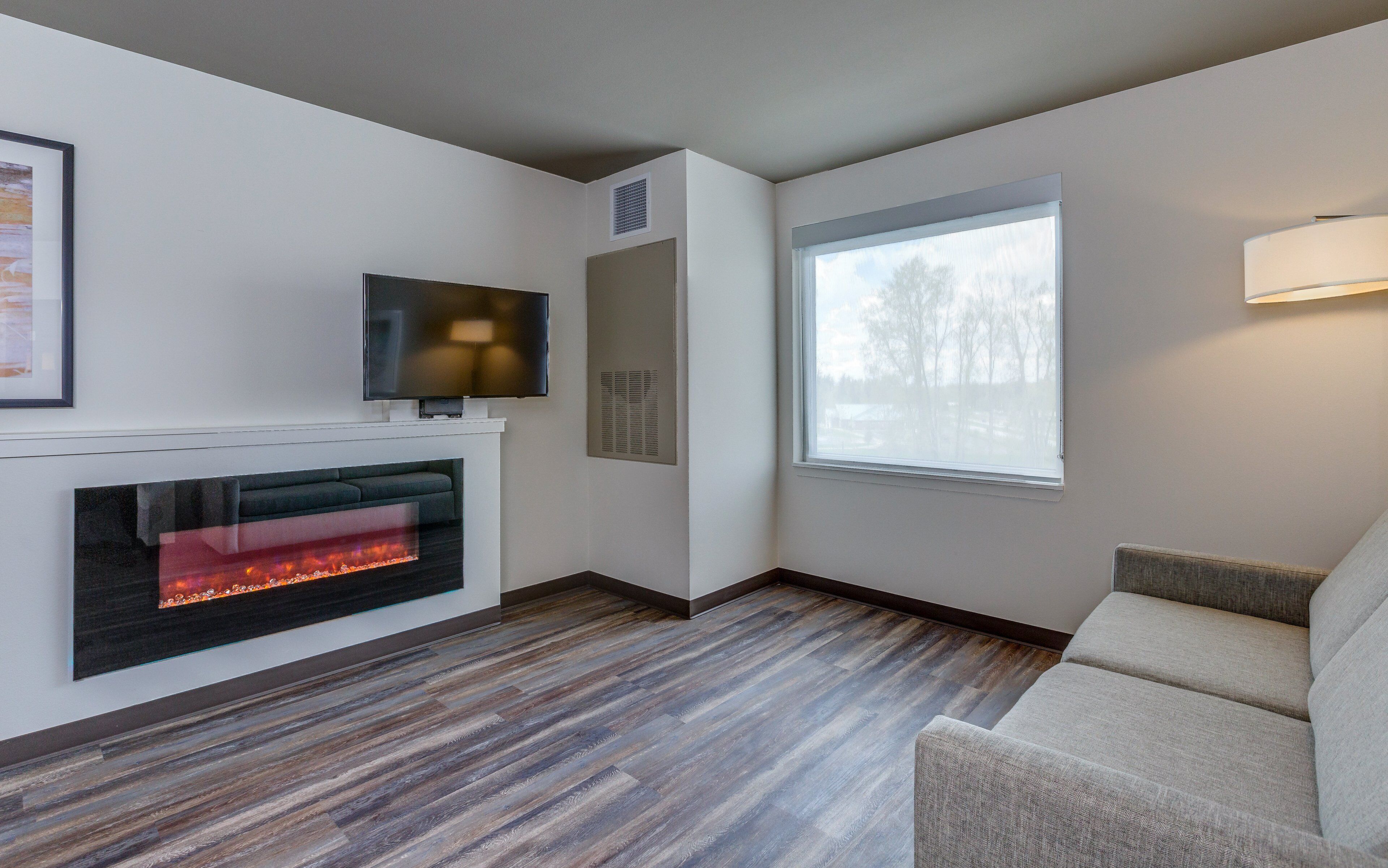 A modern living room with a fireplace, a flat-screen TV, a large window, and a sofa.