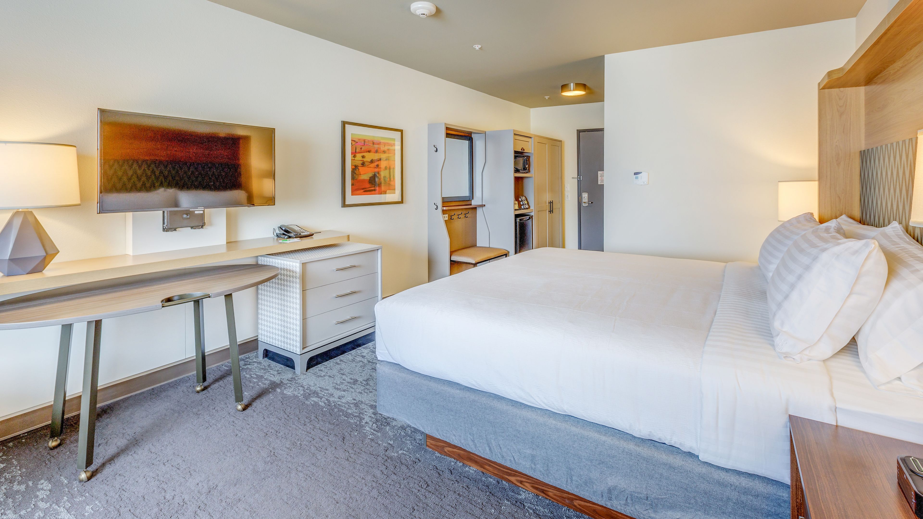 A hotel room with a bed, desk, chair, and a small seating area.