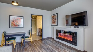 A modern living room with a fireplace, a dining area with a table and chairs, and a TV mounted on the wall.