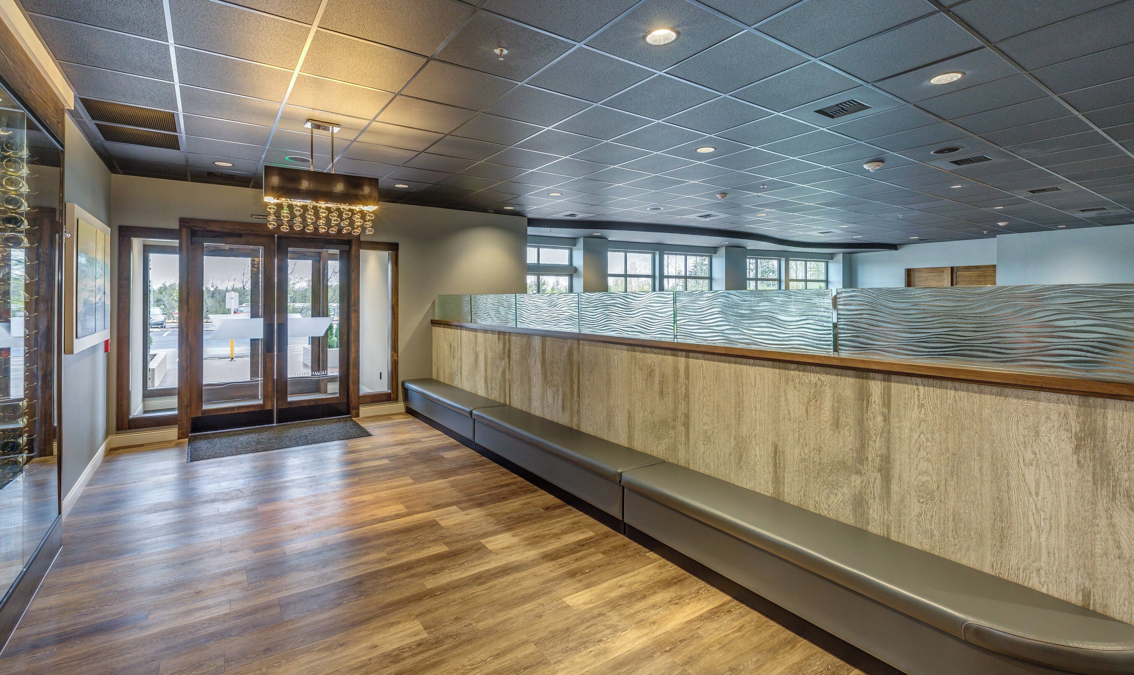 A reception area with a wooden bench, a glass partition, and a ceiling with recessed lighting.