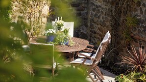 A round wooden table with four chairs, surrounded by greenery and a stone wall. - The Old Coach House (Ripon)