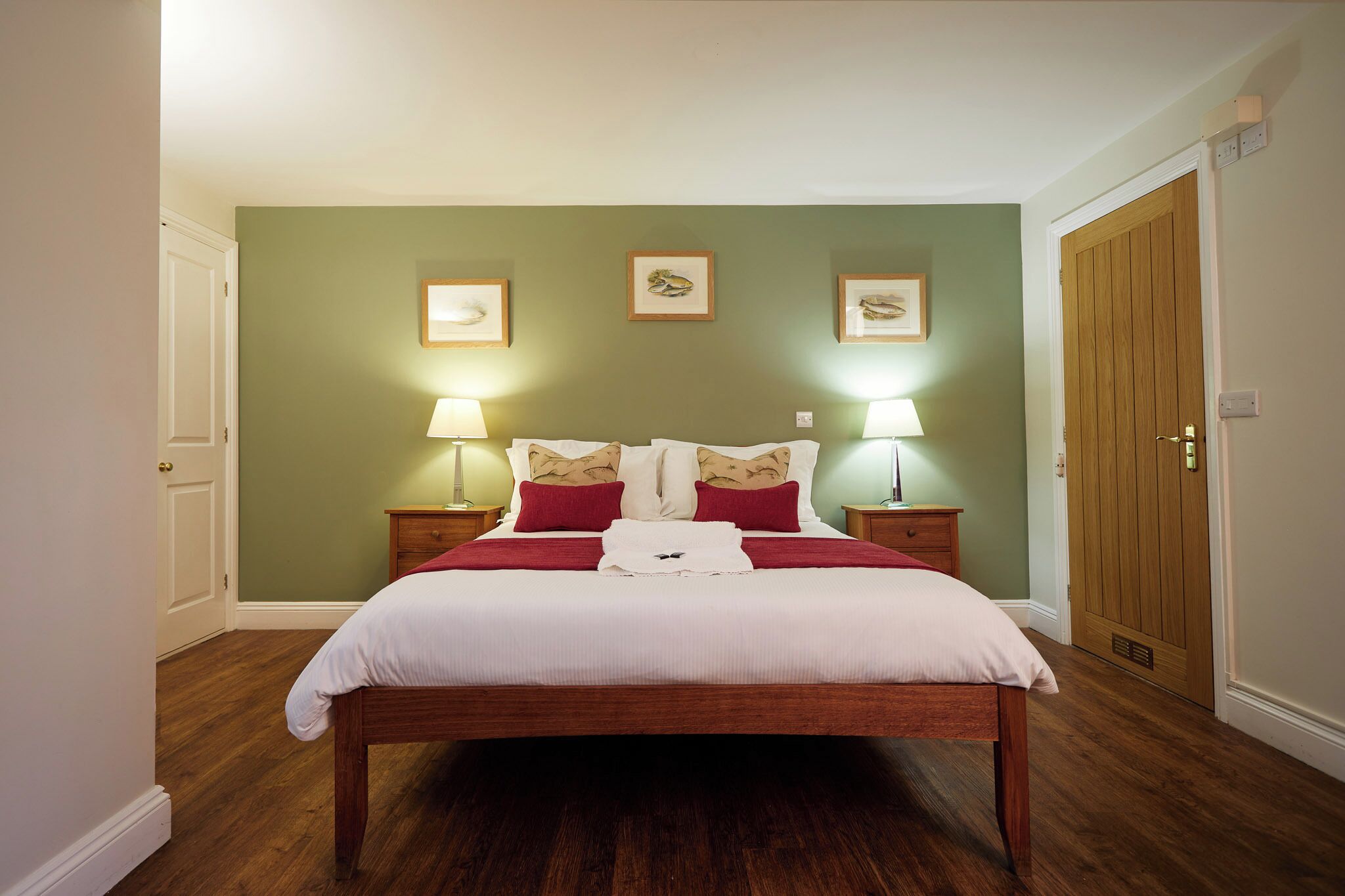 Een net opgemaakt bed met wit en rode beddengoed, twee bedlampen en lijstwerk aan de muur.