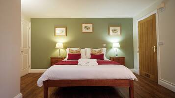 Een net opgemaakt bed met wit en rode beddengoed, twee bedlampen en lijstwerk aan de muur.