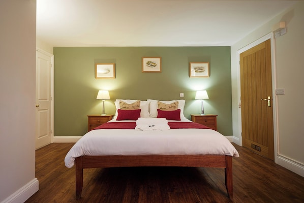 Una cama bien hecha con ropa de cama blanca y roja, dos lámparas de noche y cuadros en la pared.