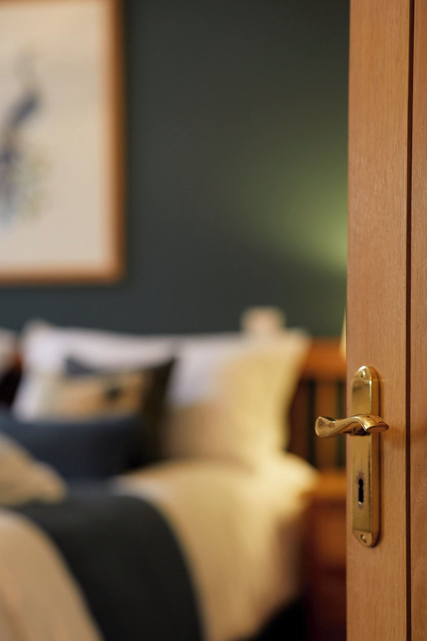 A wooden door with a brass handle, a bed with a white and black bedspread, and a framed picture on the wall.