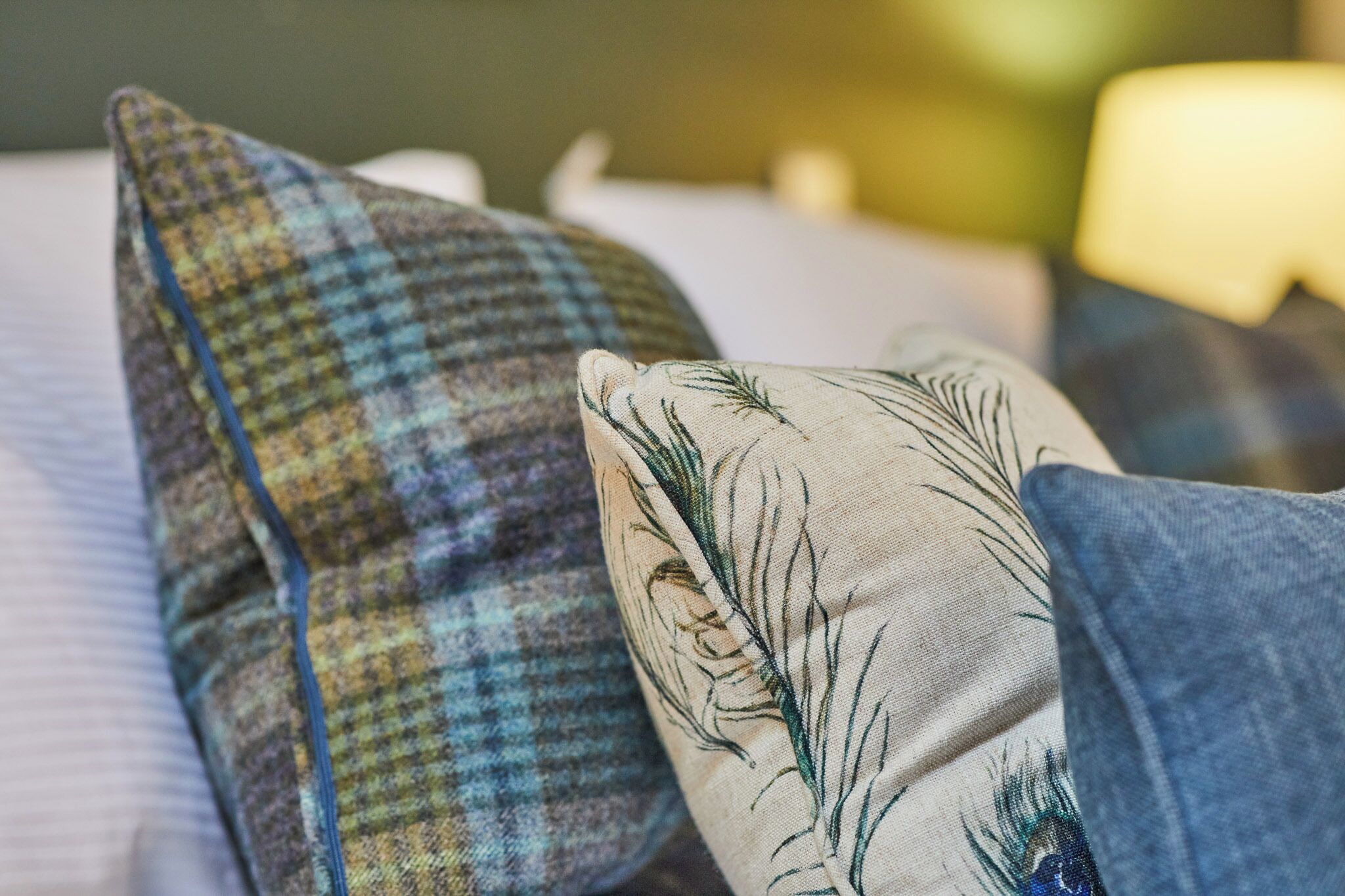 A bed with a plaid pillow and a pillow with a feather design.