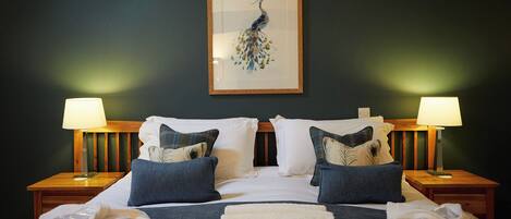 A hotel room with a large bed, two nightstands, two lamps, and a framed peacock artwork on the wall.