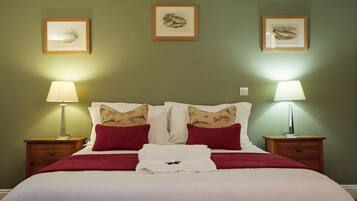 Una cama bien hecha con decoración en blanco y rojo, flanqueada por dos mesitas de noche con lámparas, y una obra de arte en la pared.