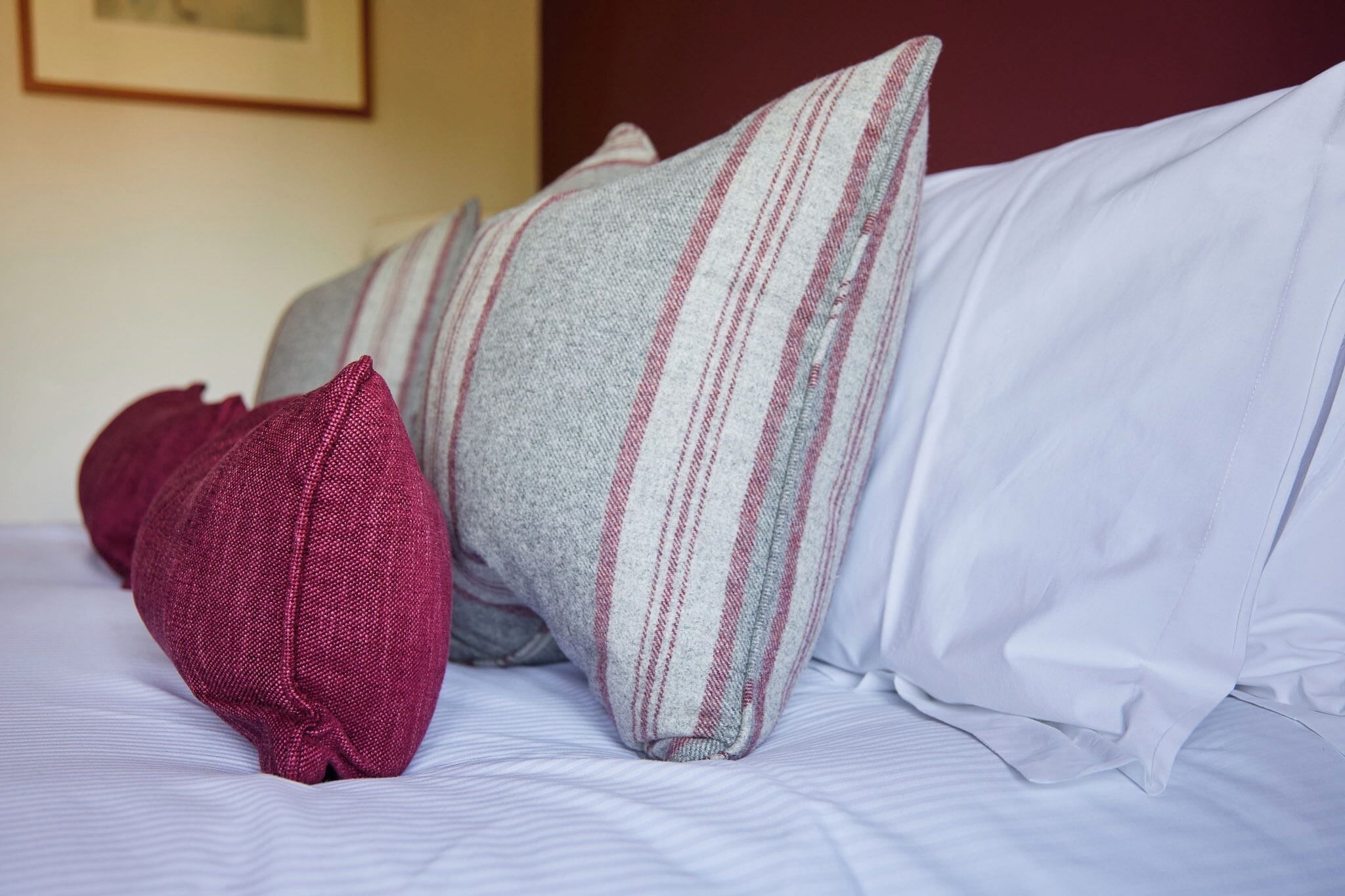 Uma cama com travesseiros listrados e um travesseiro vermelho liso.