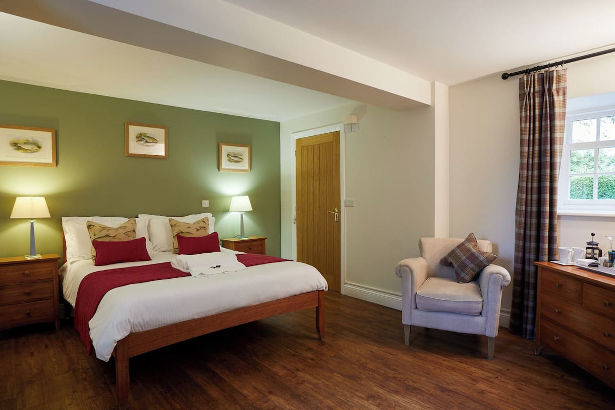 A neatly arranged bedroom with a wooden bed, two bedside tables with lamps, a chair, a dresser, and a window with curtains.