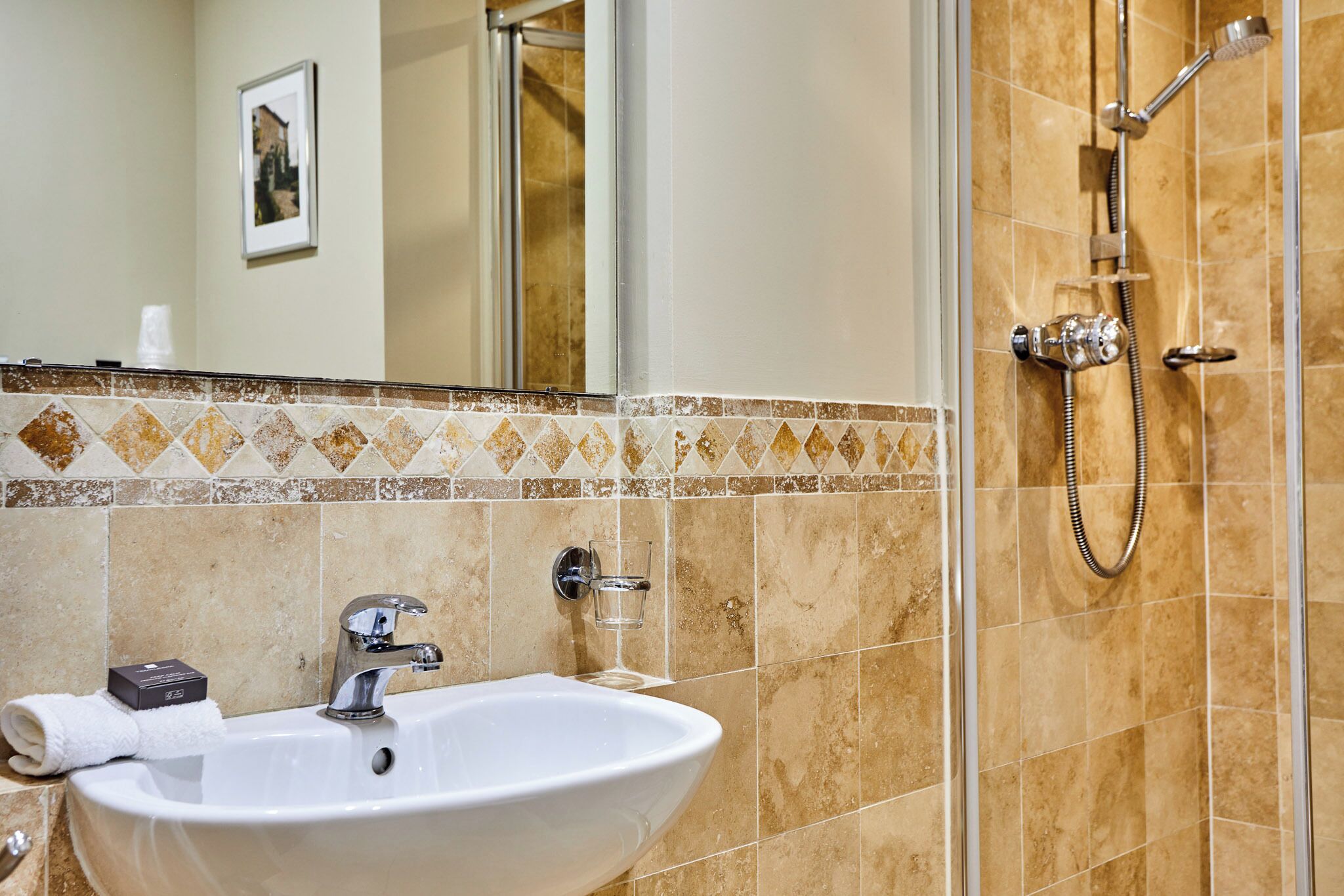 Ein Badezimmer mit Waschbecken, Spiegel, Dusche und gefliesten Wänden.