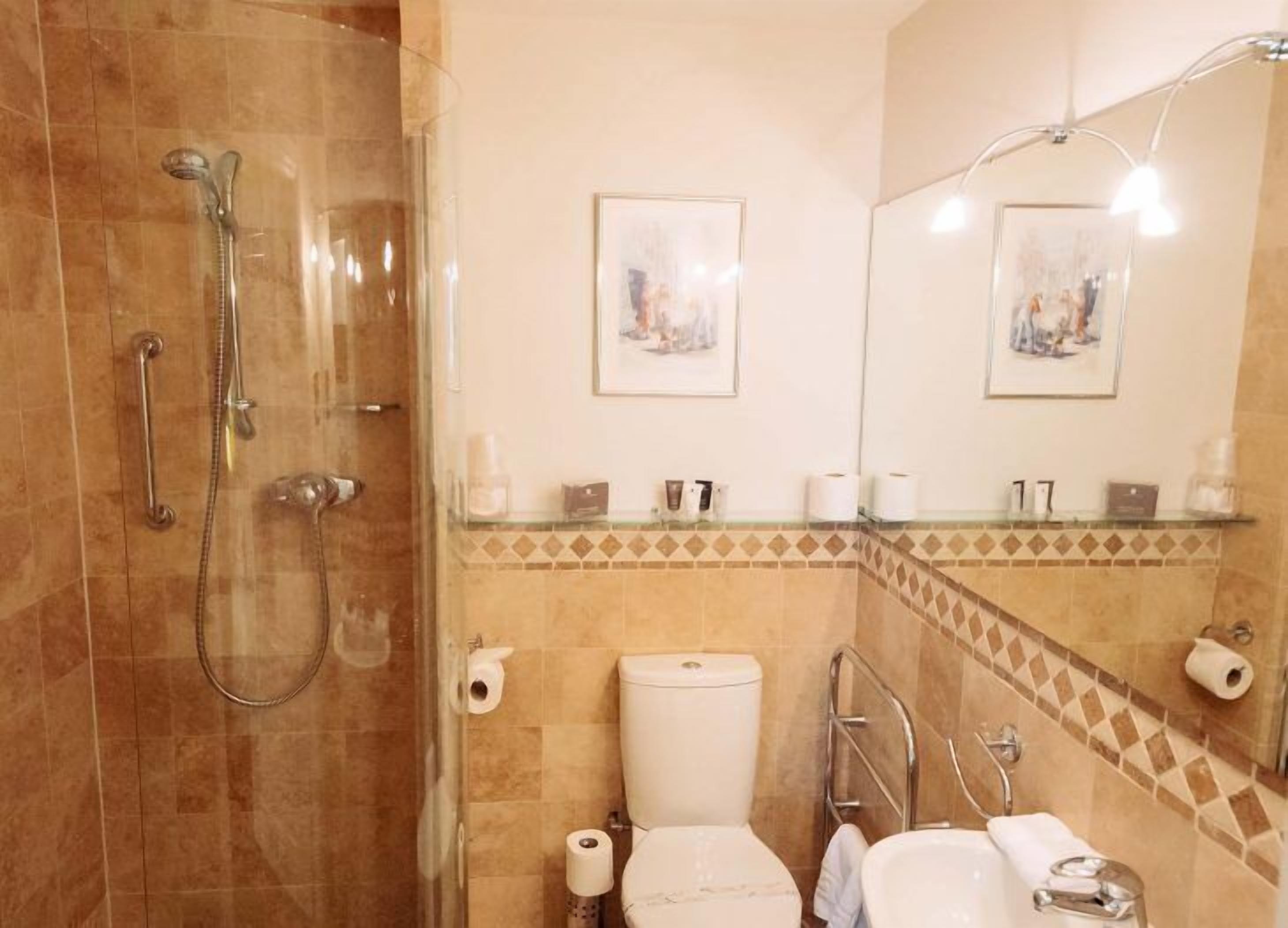 Un bagno con doccia vetrata, un water, un lavandino e uno specchio con due quadri incorniciati.
