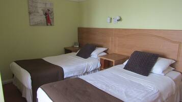 A hotel room with two single beds, a wooden headboard, a nightstand with a lamp, and a wall clock.