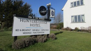 Une enseigne pour l’hôtel Hunters Lodge, indiquant les services proposés, notamment l’hébergement avec petit-déjeuner, les repas au bar, les cappuccinos, l’organisation de mariages et la mise à disposition d’une salle de réception.