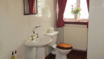 A bathroom with a white sink, a mirror, a toilet with a wooden seat, and a window with red curtains.