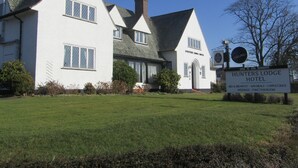 Un bâtiment blanc avec une enseigne indiquant « Hunters Lodge Hotel » et un panneau publicitaire pour la bière « Carling ».
