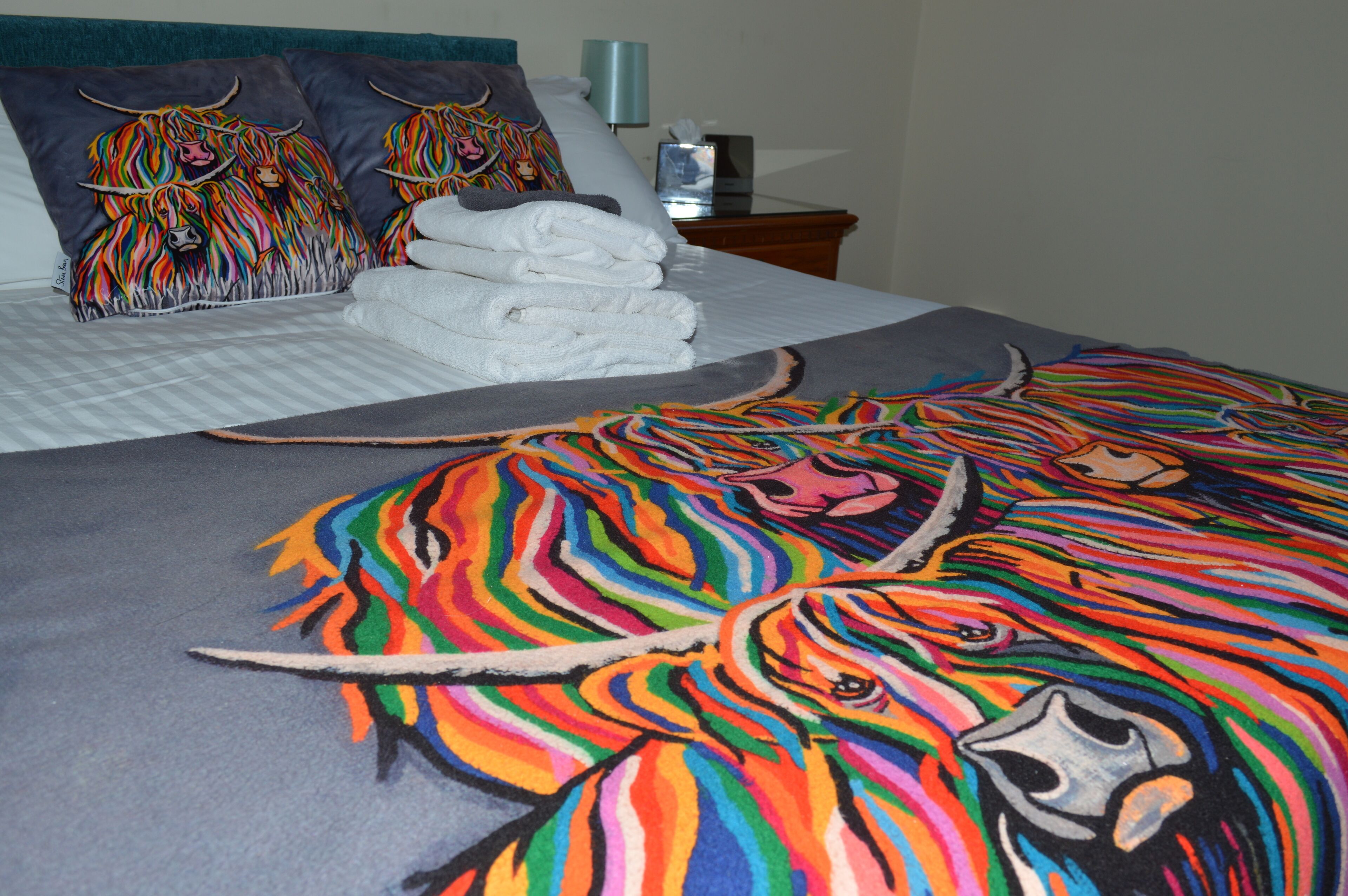 A bed with a colorful blanket, pillows with animal designs, and neatly folded white towels.