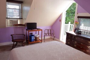A bedroom with a bed, a wooden chair, a desk with a computer, a dresser, and a window with blinds.