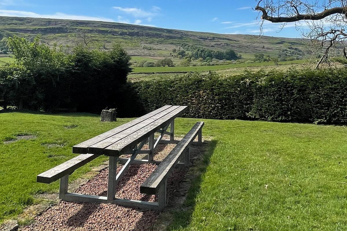 A picnic table in a grassy field with a view of rolling hills in the background.