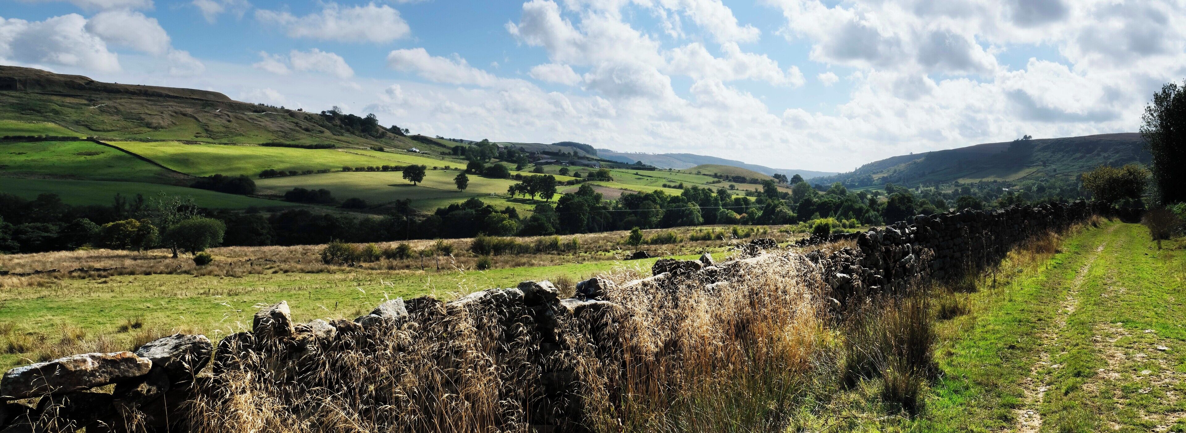 A stone wall with a grassy field and rolling hills in the background.