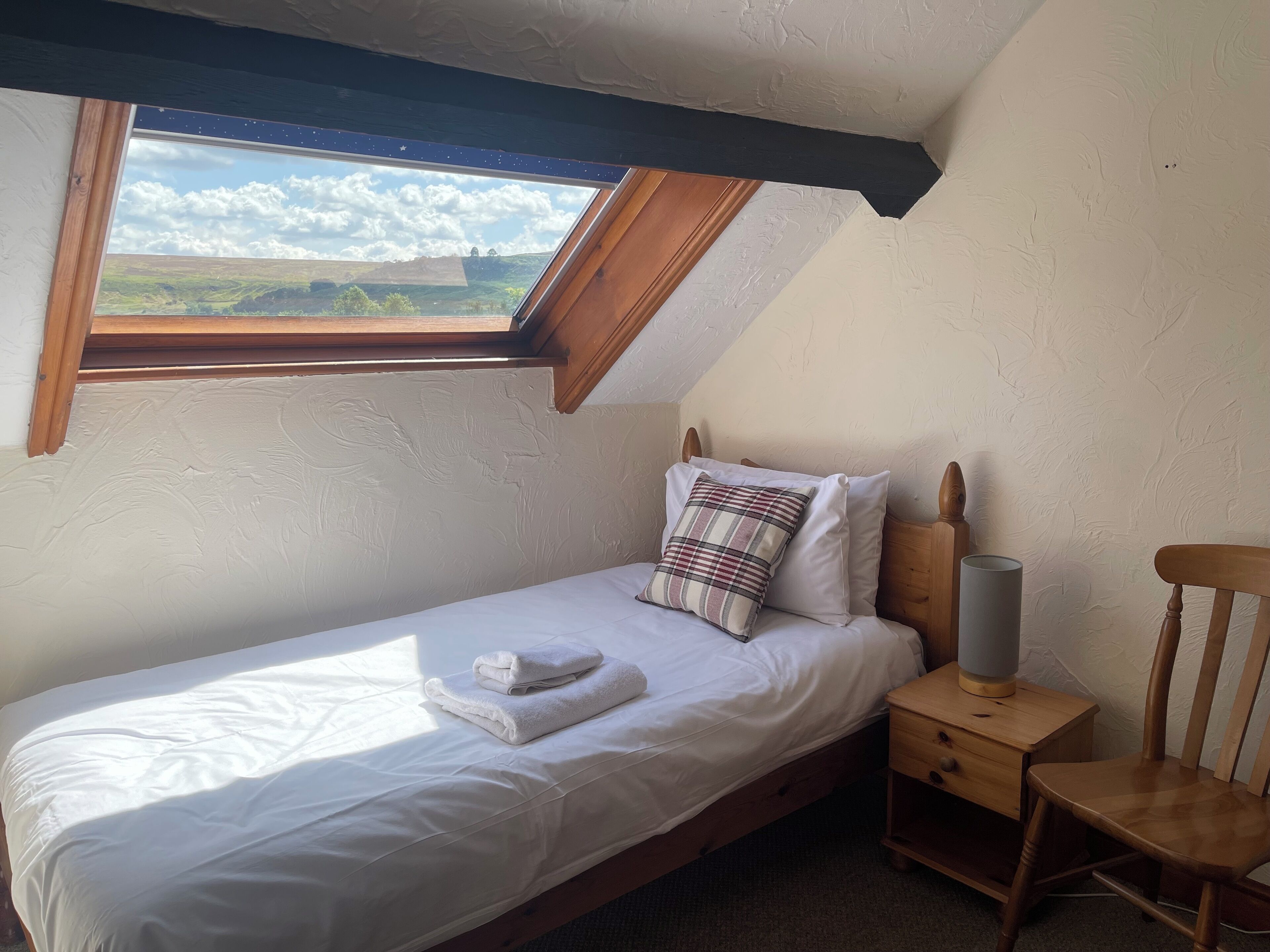 Een knus slaapkamer met een eenpersoonsbed, nachtkastje, stoel en dakraam.