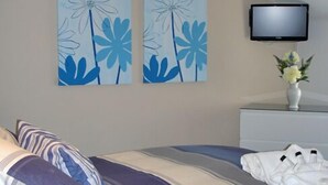 A hotel room with a bed, pillows, a flat-screen TV, and two wall-mounted paintings. - South Beach Apartments (Blackpool)