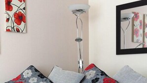 A modern living room with a grey sofa, floral-patterned cushions, a metallic sculpture on a black table, and a tall floor lamp. - South Beach Apartments (Blackpool)