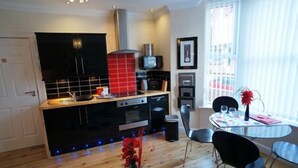 A modern kitchen with black cabinets, a red tiled backsplash, and a dining area with a table and chairs. - South Beach Apartments (Blackpool)