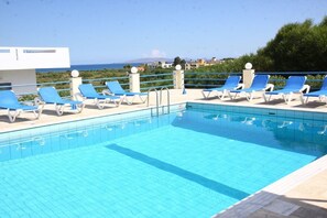 A swimming pool with blue lounge chairs and a view of the sea. - Poseidon Hotel (Malevizi)