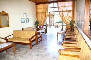 A hotel lobby with a long reception desk, several wooden chairs, and a large window with curtains. - Poseidon Hotel (Malevizi)