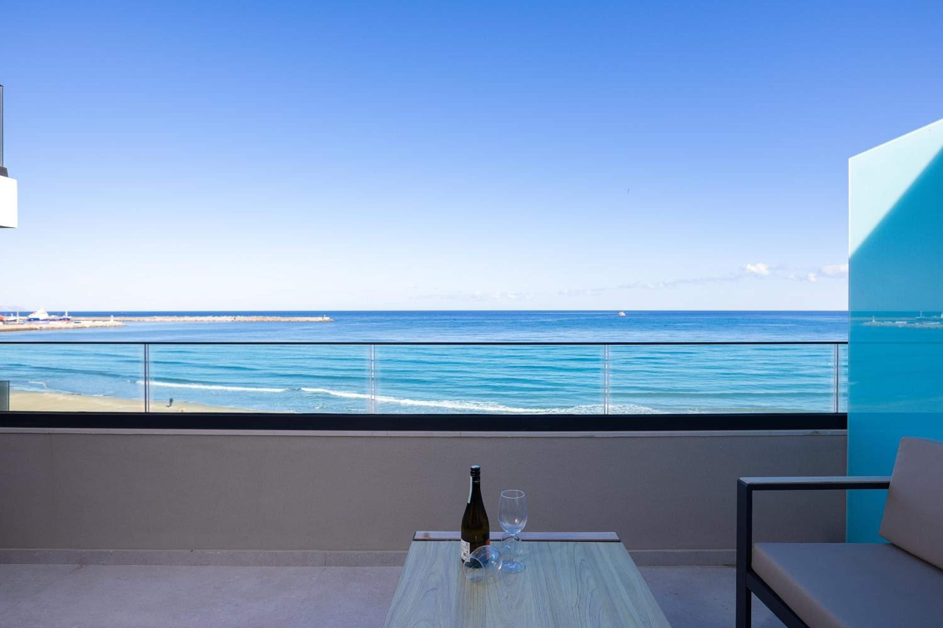 A balcony with a view of the sea, a bottle of wine, and a glass on a table.