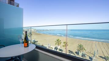 A balcony with a table, a bottle of wine, and a glass. The view includes a beach and the ocean.