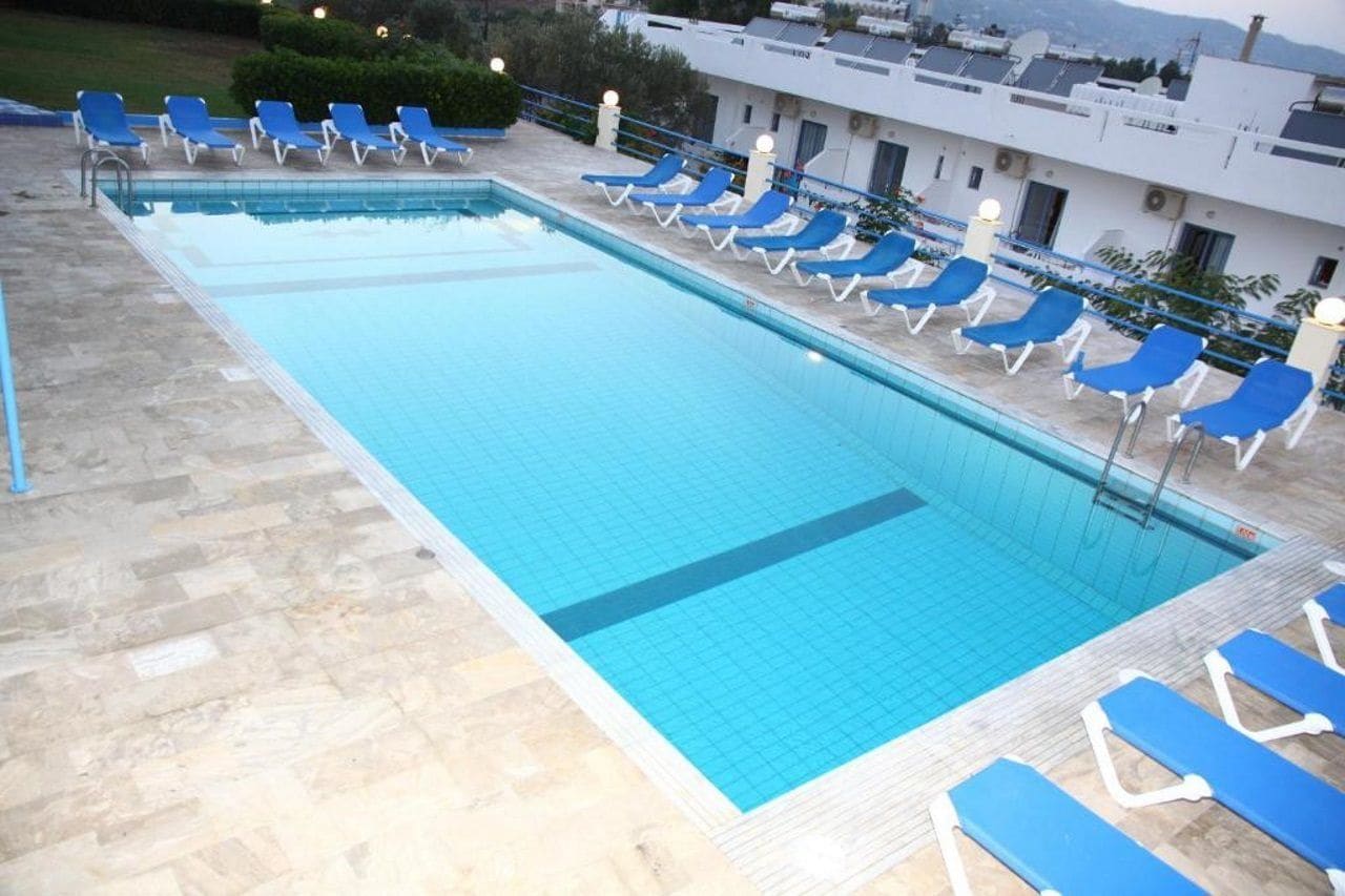 A rectangular swimming pool with a tiled edge, surrounded by blue lounge chairs and a stone deck.