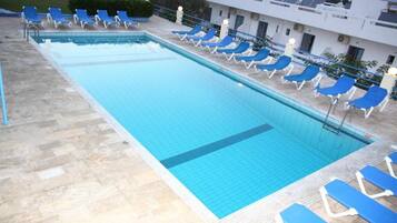 A rectangular swimming pool with a tiled edge, surrounded by blue lounge chairs and a stone deck.