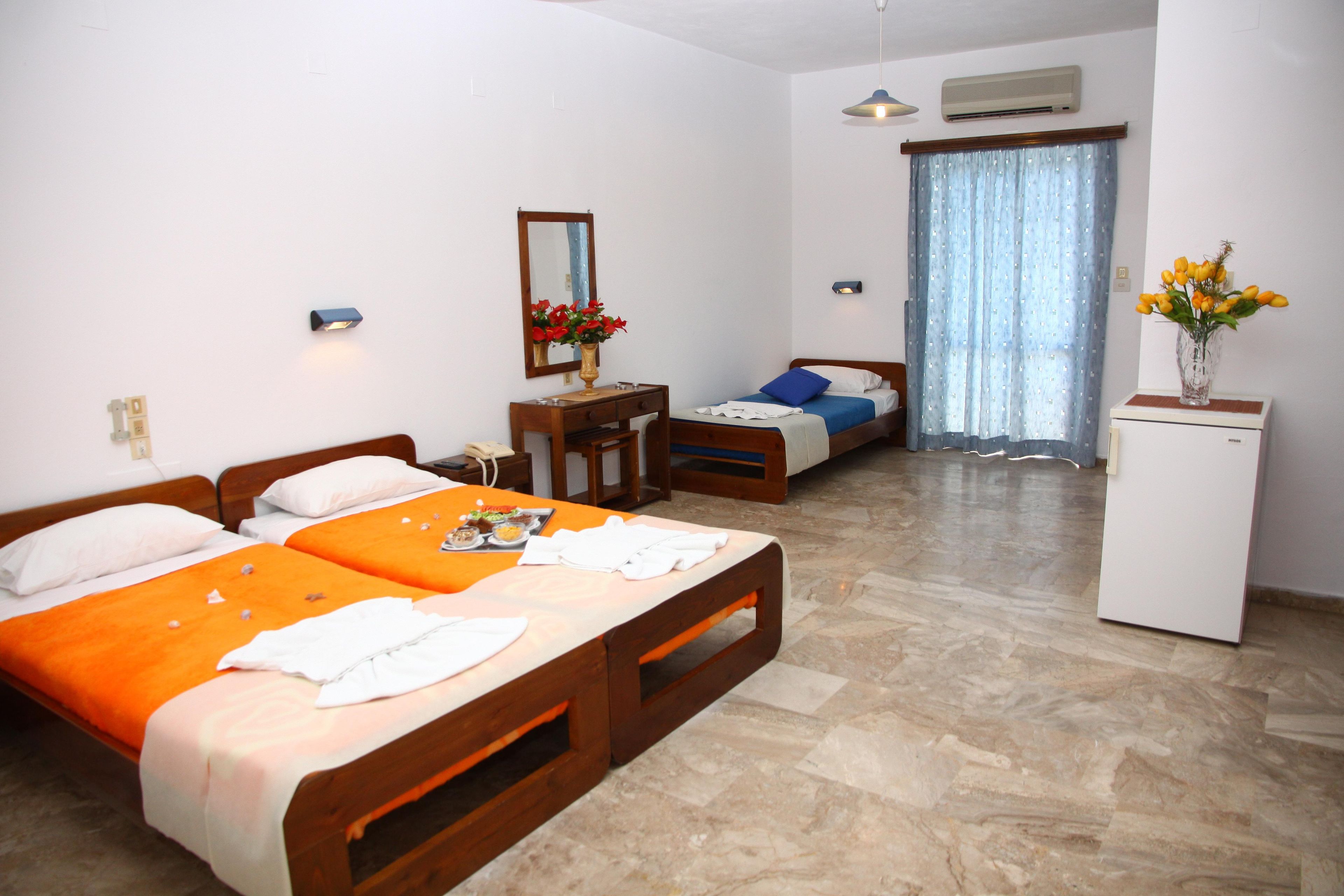 A hotel room with two beds, a desk, a mirror, a vase with flowers, and a window with curtains.