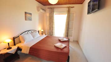 Un dormitorio con cama, dos lámparas de noche, un cuadro en la pared, una ventana con cortinas y un televisor montado.
