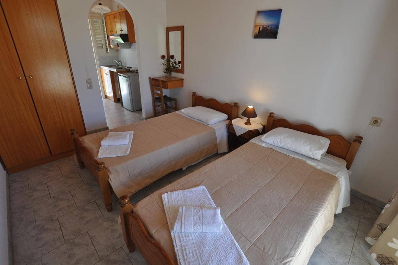 A hotel room with two beds, a desk, a chair, a mirror, and a small table with a lamp.