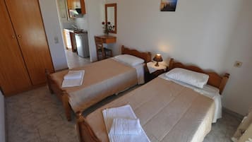 A hotel room with two beds, a desk, a chair, a mirror, and a small table with a lamp.