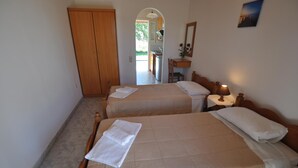 A hotel room with two beds, a wooden wardrobe, a desk with a lamp, and a view of the outdoor area.