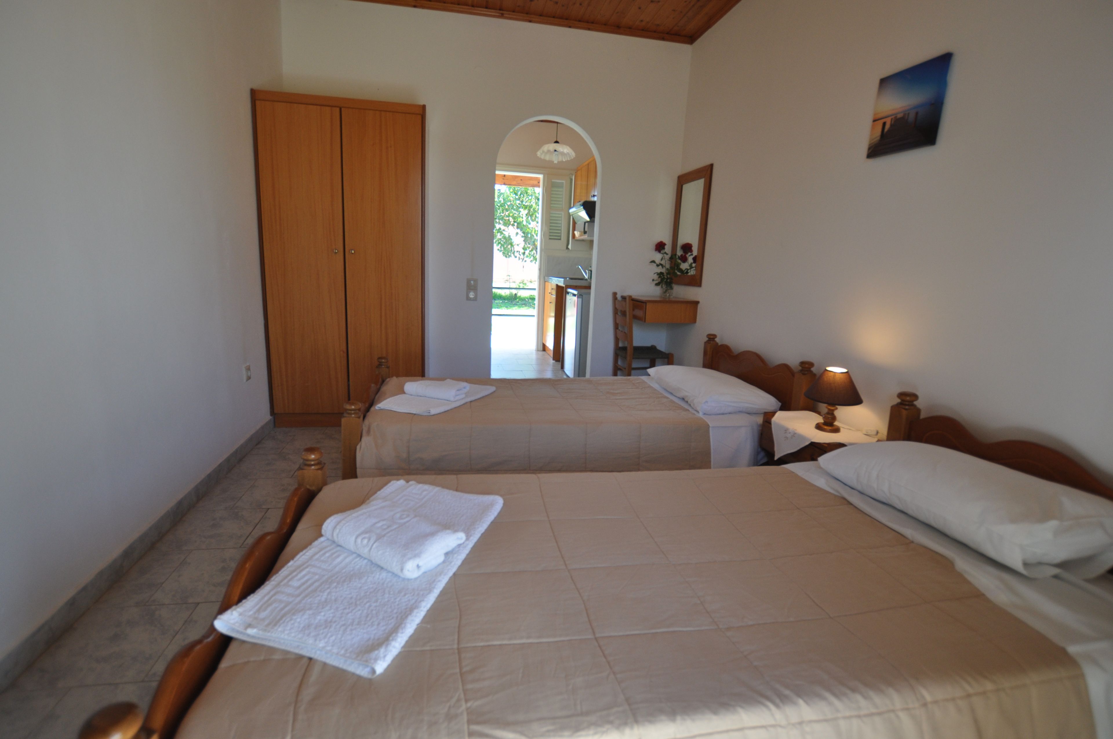 Habitación de hotel con dos camas, un armario de madera, un escritorio con lámpara y vistas al exterior.