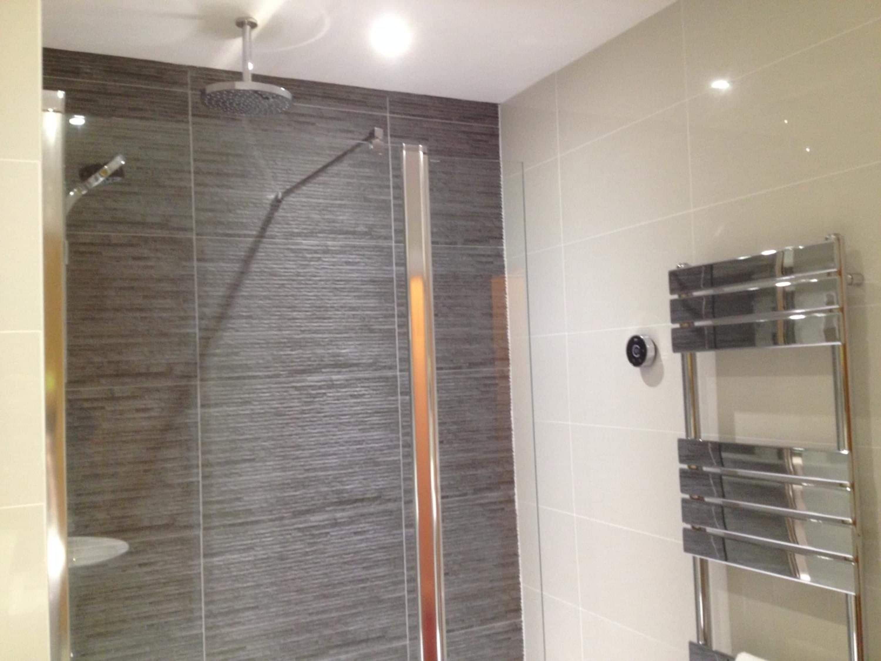 A modern bathroom with a glass-enclosed shower, a chrome towel rack, and a wall-mounted control panel.