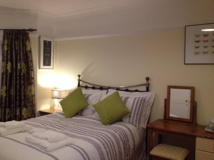 A hotel room with a bed, a bedside table, a lamp, a framed picture on the wall, and a window with curtains.