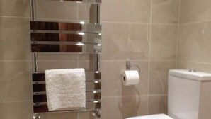 A modern bathroom with a chrome towel rack, toilet, and beige tiled walls. - LA B and B Guest Accommodation (Chichester)