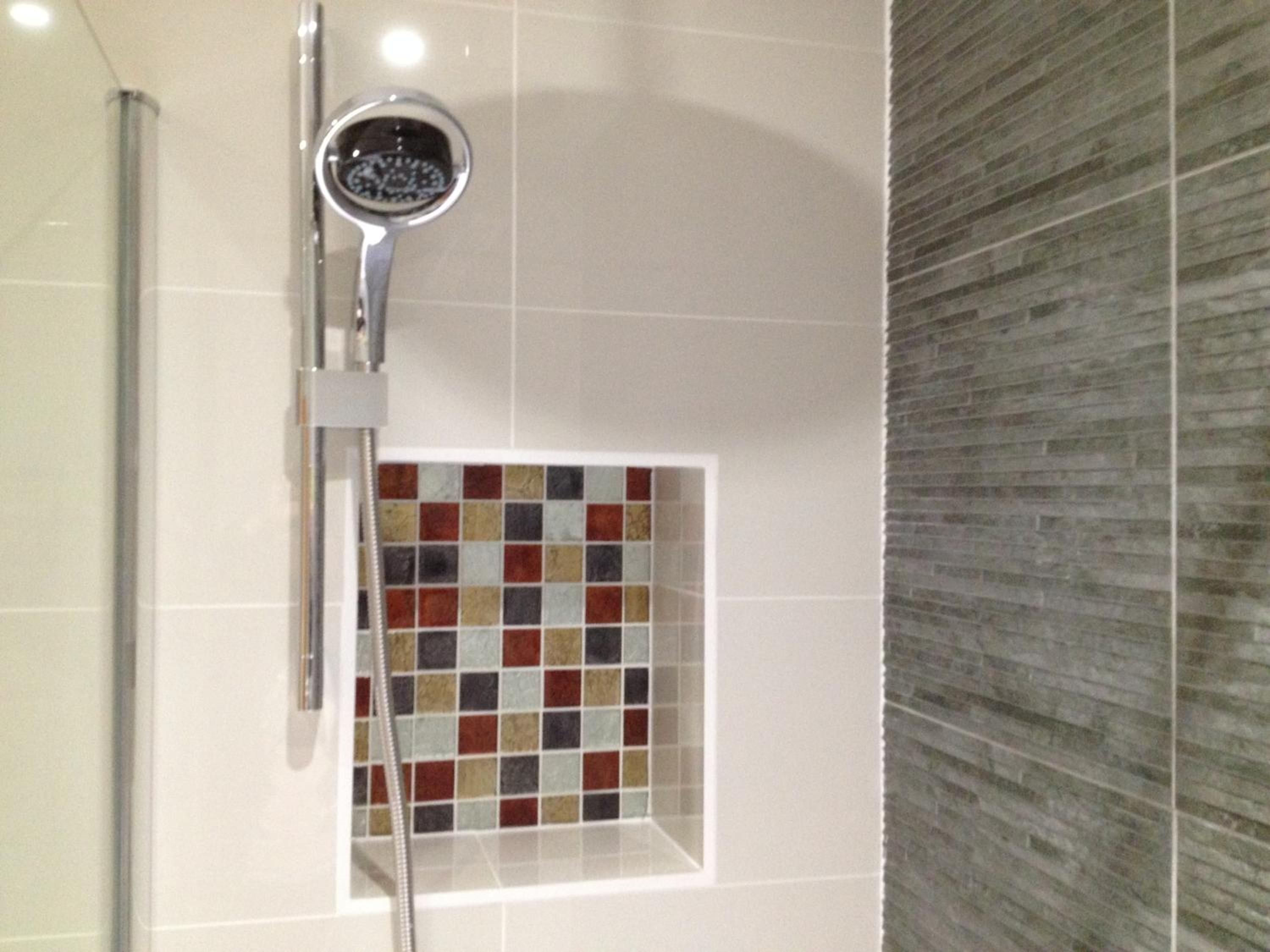 A shower with a chrome head and a tiled wall.