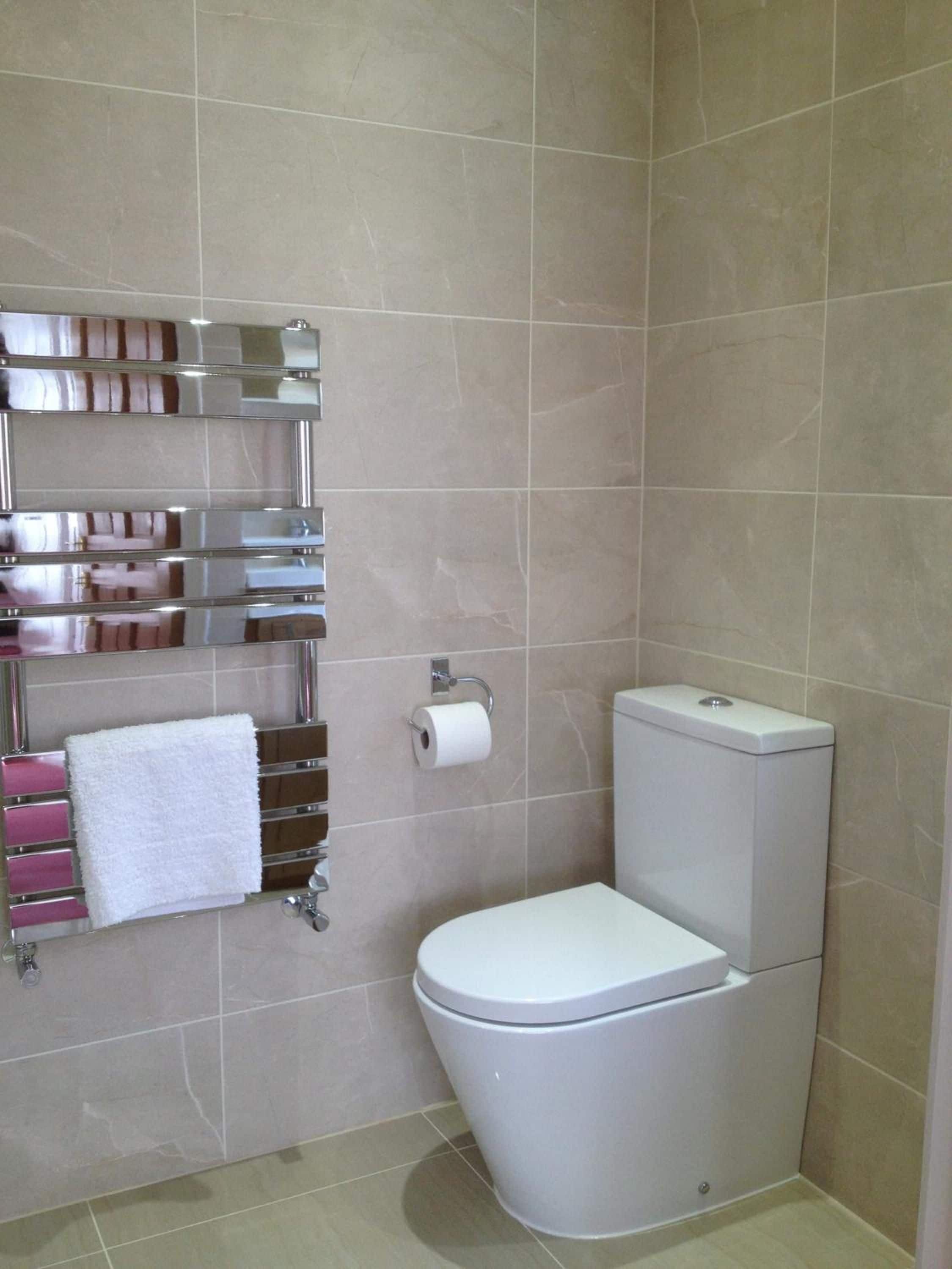 Ein Badezimmer mit Toilette, Handtuchhalter und weißen Handtüchern sowie einem Toilettenpapierhalter.