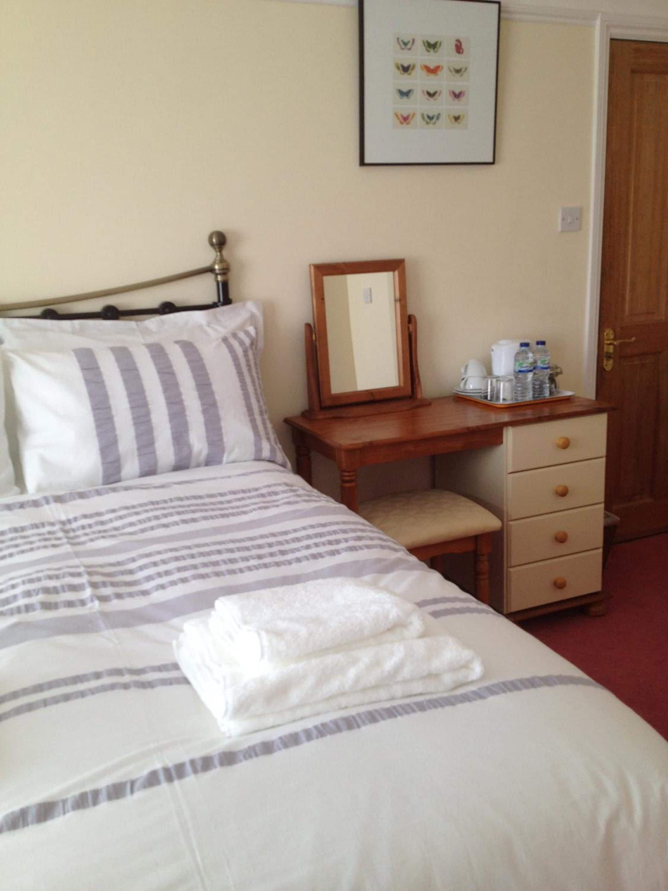 A hotel room with a bed, a bedside table with a mirror, a chair, a dresser, and a framed picture on the wall.